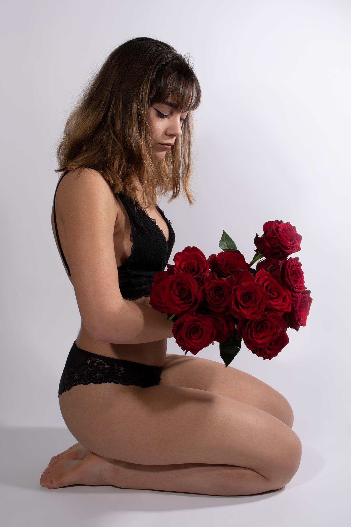 Modèle en lingerie, agenouillée, un bouquet de roses dans les mains.