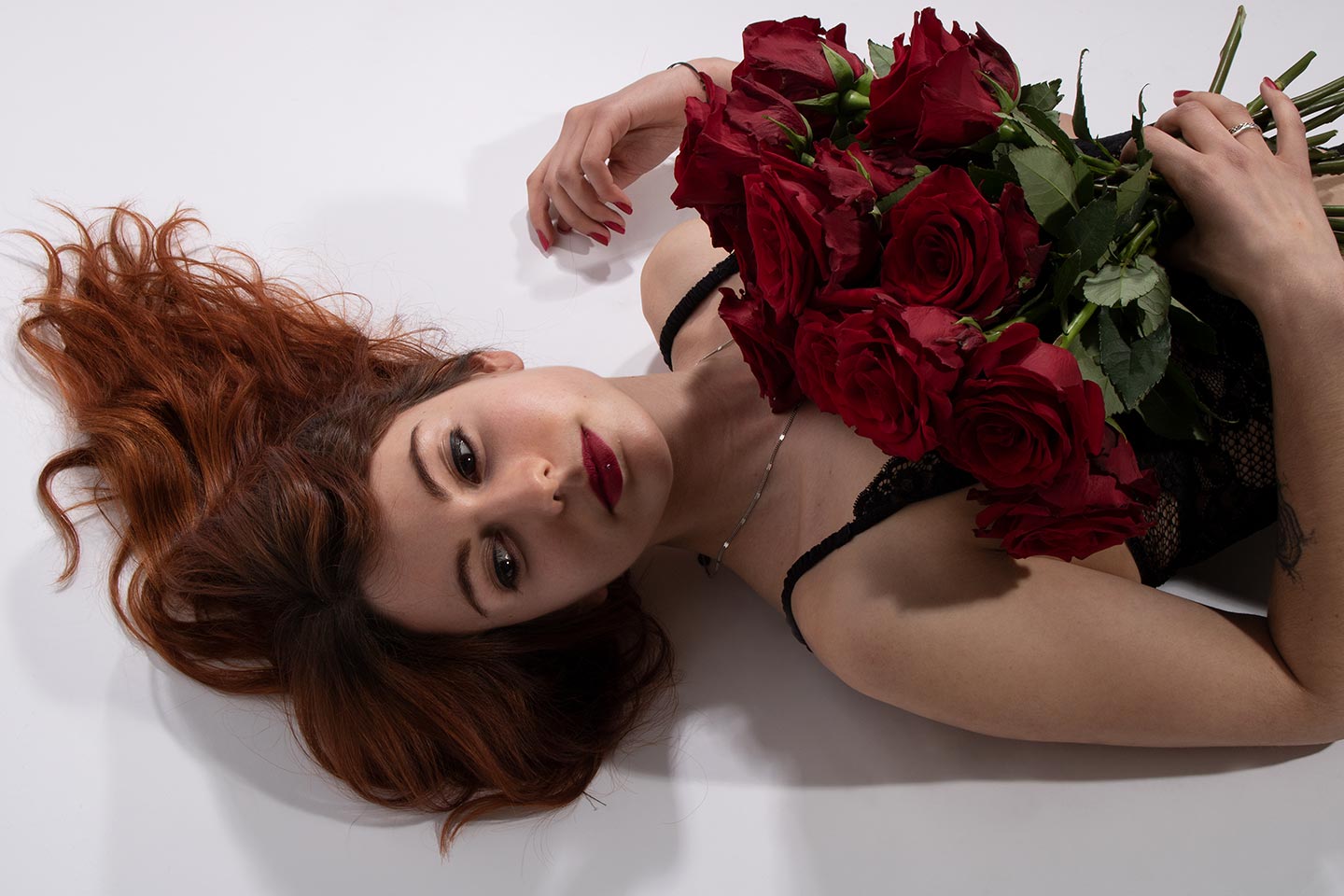 Modèle en lingerie, couchée, un bouquet de roses sur la poitrine.