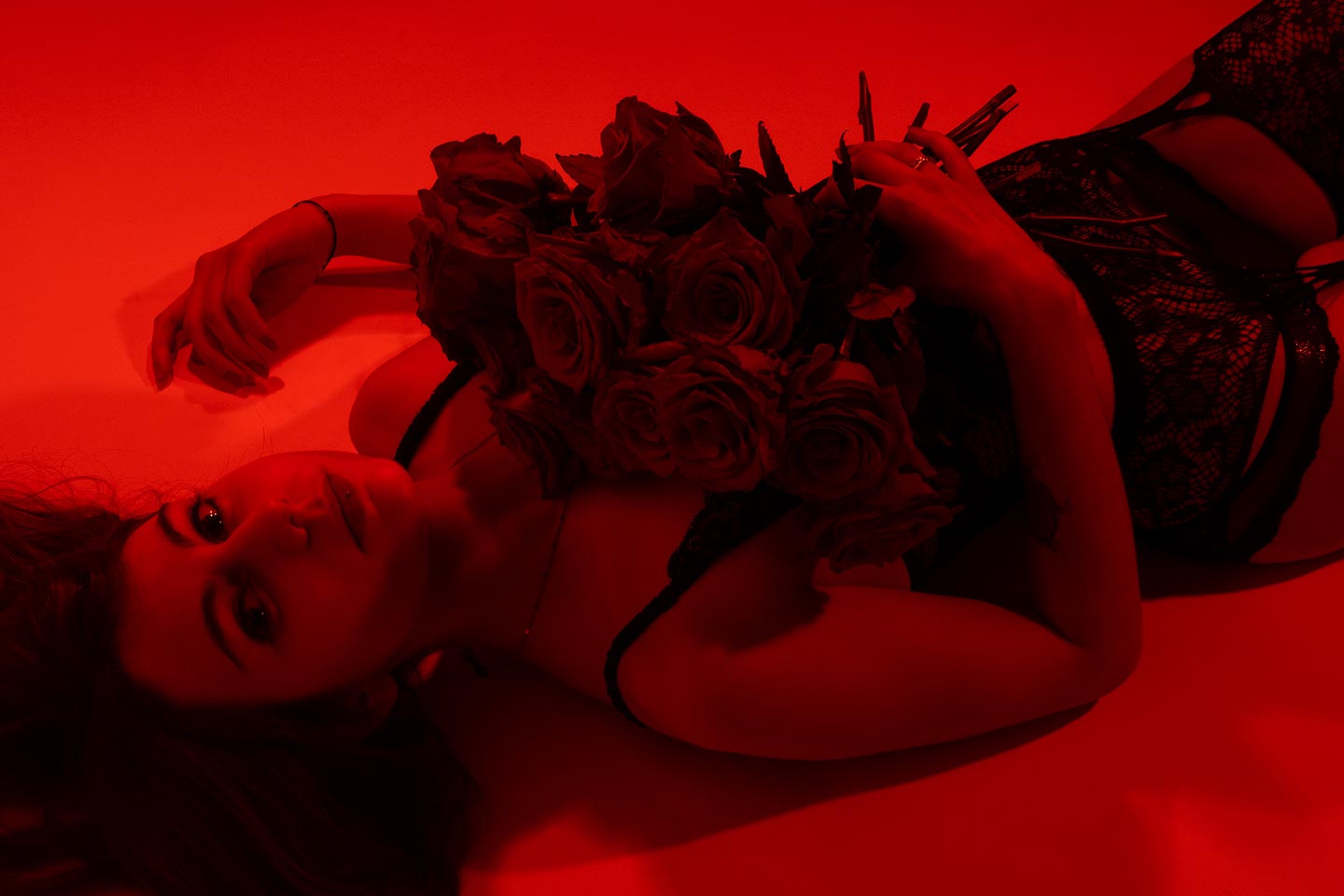 Modèle en lingerie tenant un bouquet de roses dans un éclairage rouge intense.